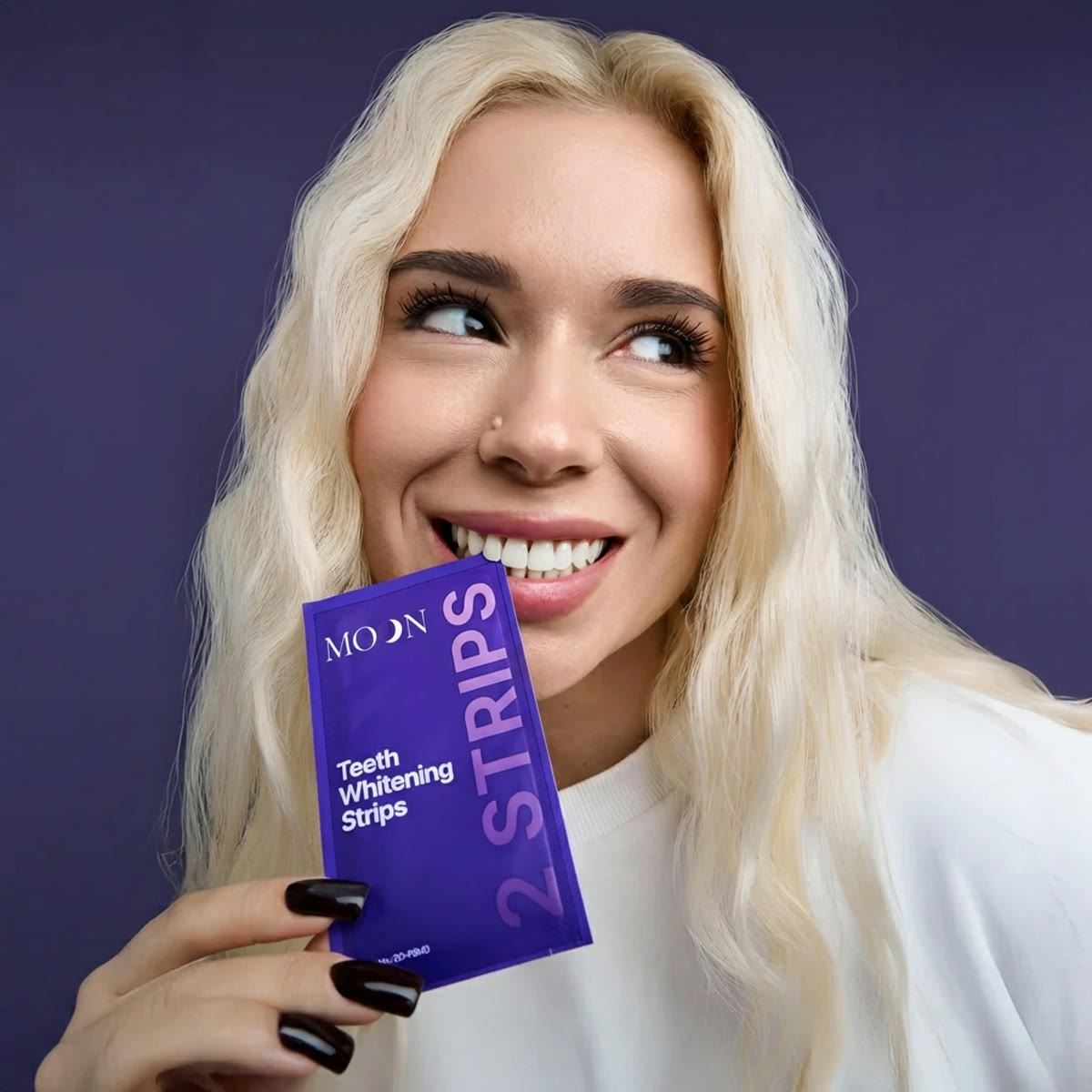 A woman smiling with a pack of MOON purple whitening strips